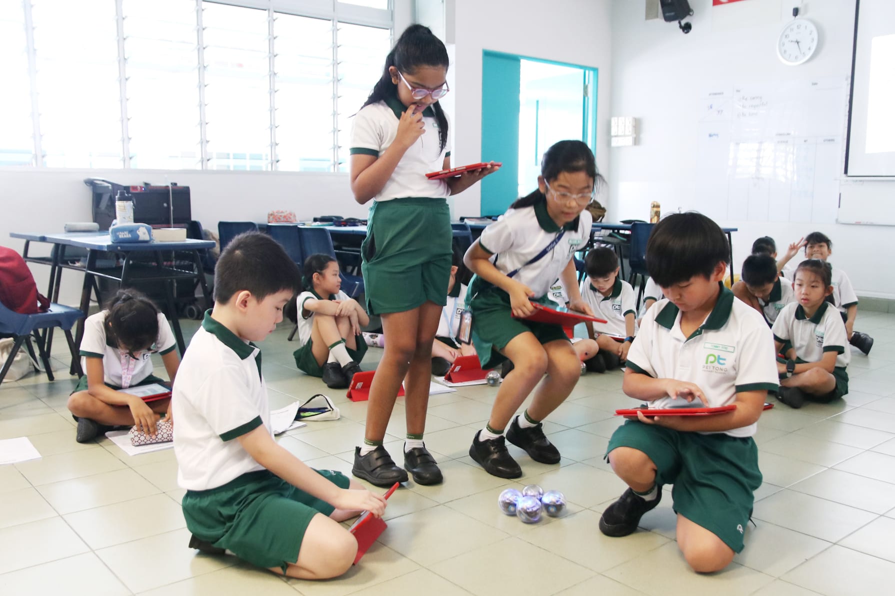 Students collaborate in small groups using tablets and coding robots, exploring computational thinking through hands-on programming challenges.
